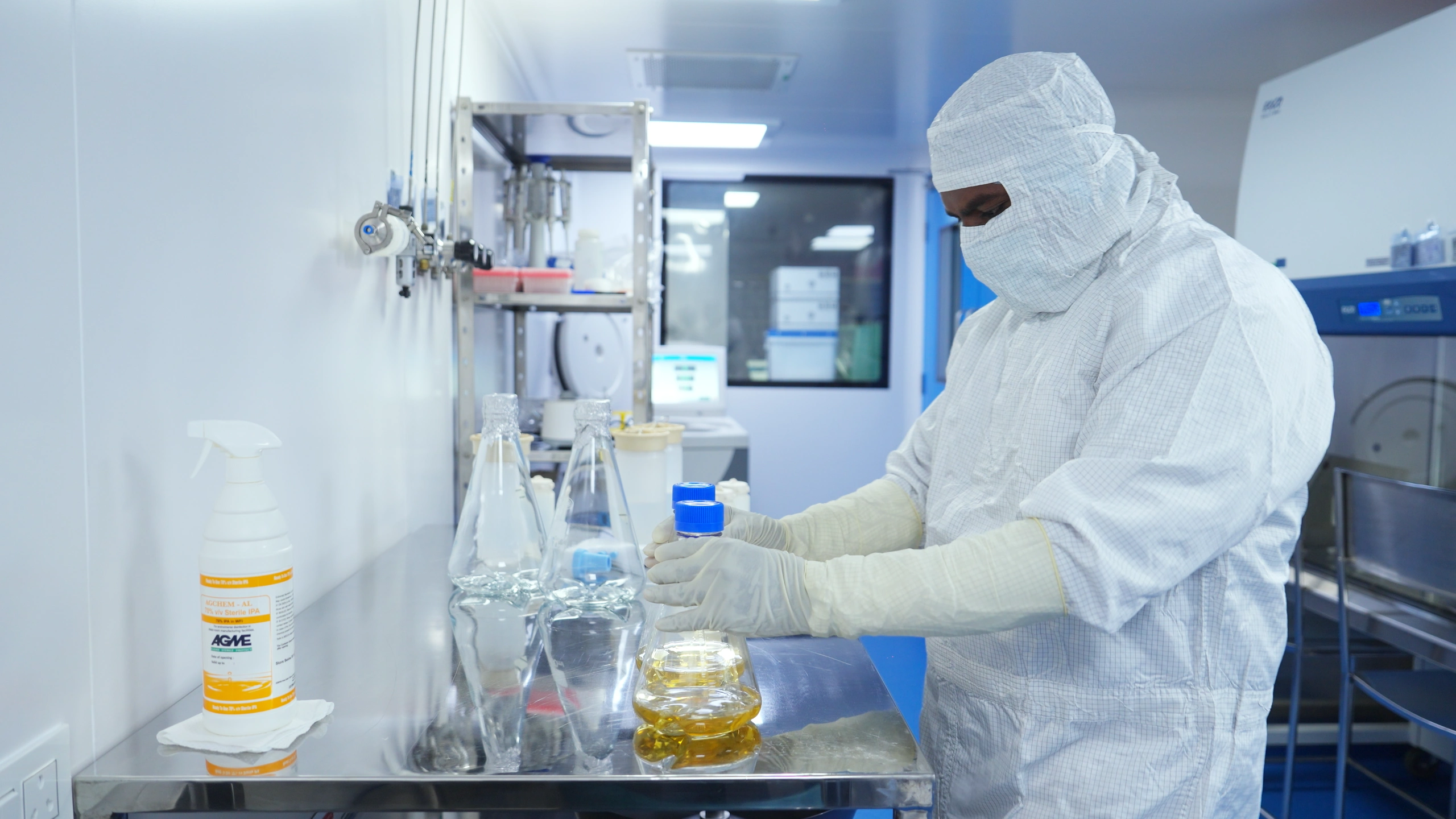 An operator handling flasks of media at a cleanroom bench.